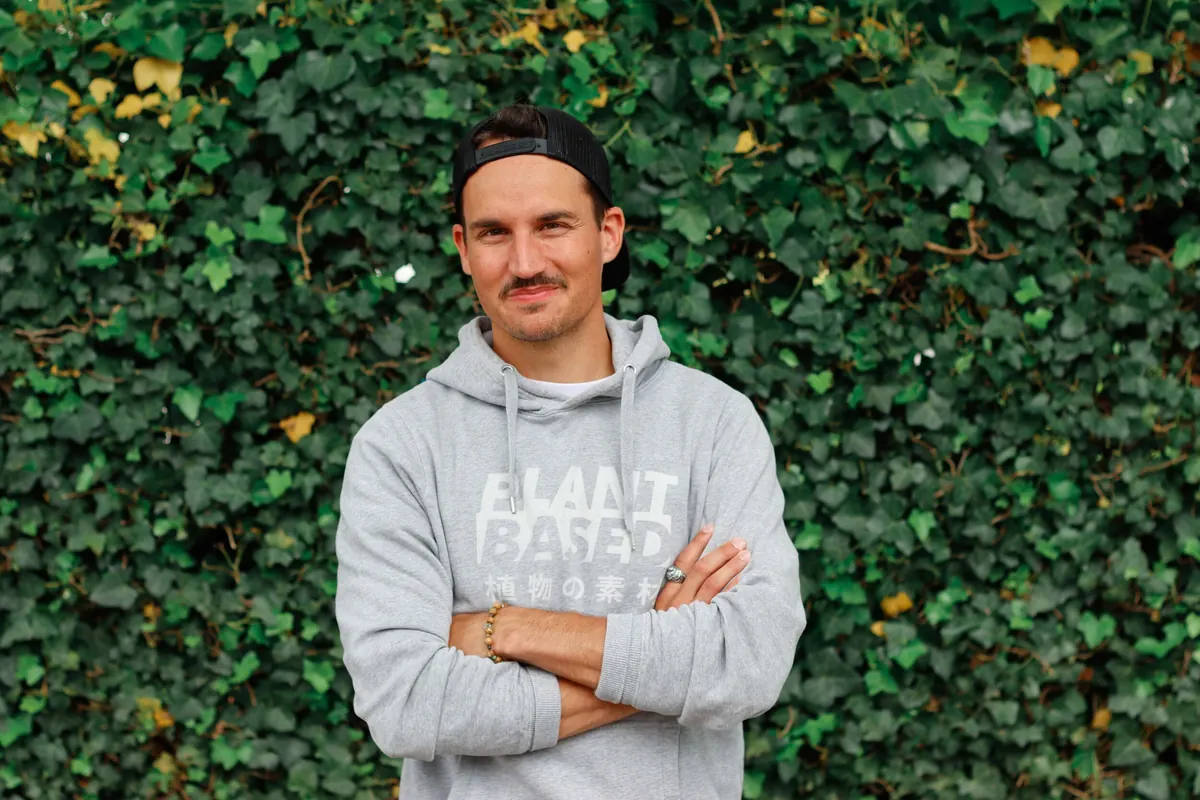 Fabian Zbinden mit verschränkten Armen vor einer efeubewachsenen Wand